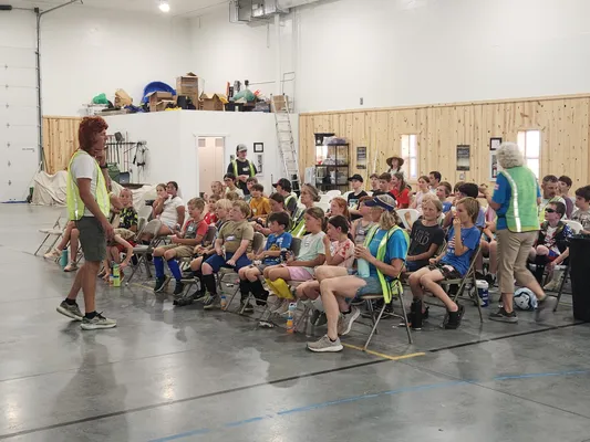 Coach in a safety vest speaking to a large group of seated campers indoors