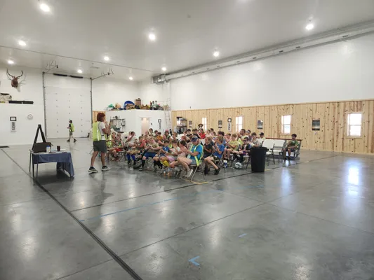 Wide view of campers seated in the gym as a coach addresses the group