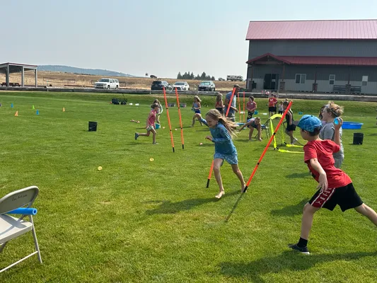 Youth running a relay course marked with cones and poles on the grass field