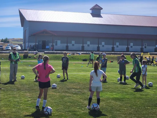 Youth practicing with soccer balls on the field as a coach looks on