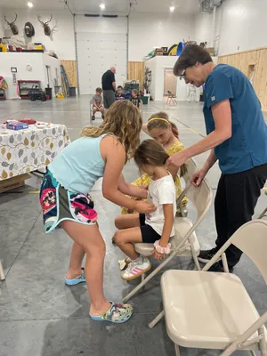 Nurse in scrubs guiding youth as they practice bandaging a seated classmate